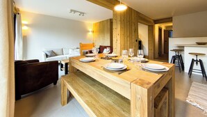 Een houten eettafel gedekt met borden en glazen, een bank en een lange houten bank in een kamer met houten balken en een hanglamp.