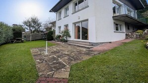 Ein modernes, zweistöckiges Haus mit einer Steinterrasse, einer Holzterrasse und einem gepflegten Rasen.