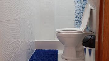 Ein Badezimmer mit weißen, strukturierten Wänden, einer weißen Toilette, einem blauen Duschvorhang und einer blauen Badmatte.