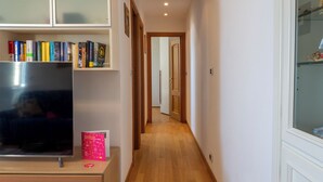 Ein schmaler Flur mit Holzdielen, einem Fernseher auf einem Schrank und einem Bücherregal voller Bücher.