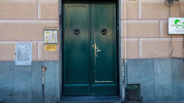 Eine grüne Doppeltür mit einer verzierten Metallverkleidung oben, einem Schild mit der Nummer 51 und einem Verteilerkasten an der Wand.