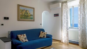 Ein Zimmer mit einem blauen Sofa, einem Gemälde an der Wand und einem Fenster mit Vorhängen.