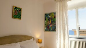 Ein Hotelzimmer mit einem Bett, einem Nachttisch mit Lampe, zwei Bildern an der Wand und einem Fenster mit Vorhängen.