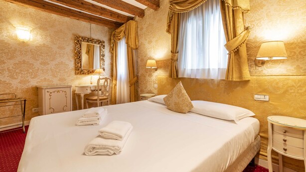 Une chambre d’hôtel avec un grand lit, un bureau avec une chaise, un miroir et deux lampes fixées au mur.
