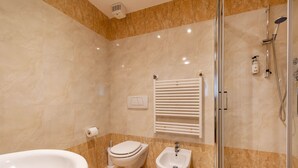 Une salle de bain moderne équipée d’une baignoire, de toilettes, d’un bidet et d’une douche séparée par des parois en verre.