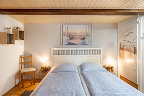 A bedroom with two beds, a wooden chair, bedside lamps, and a painting of a beach scene. - Apartment 'Möwennest' with Private Terrace, Shared Garden and Wi-Fi (Wangerland)