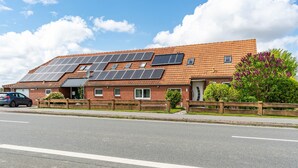 Un edificio residencial con paneles solares en el techo, un camino de entrada pavimentado y una valla de madera.