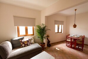 En stue med sofa, spisebord med stole, en potteplante og en hængende lampe.