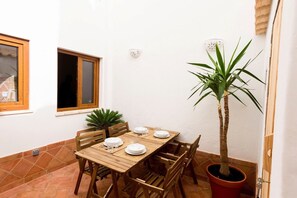 Et spisebord dækket med tallerkener og glas, omgivet af træstole, med en potteplante og et vindue på væggen.