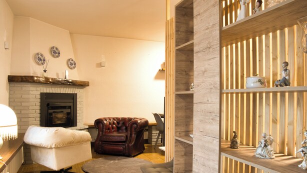 A living room with a fireplace, a leather armchair, a white armchair, a wooden shelf with figurines, and a dining area with a table and chairs. - Cozy mountain escape near Como lake (Ballabio)