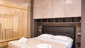 A neatly made bed with rolled towels, a wooden slat partition, and a headboard with built-in shelves. - Cozy mountain escape near Como lake (Ballabio)