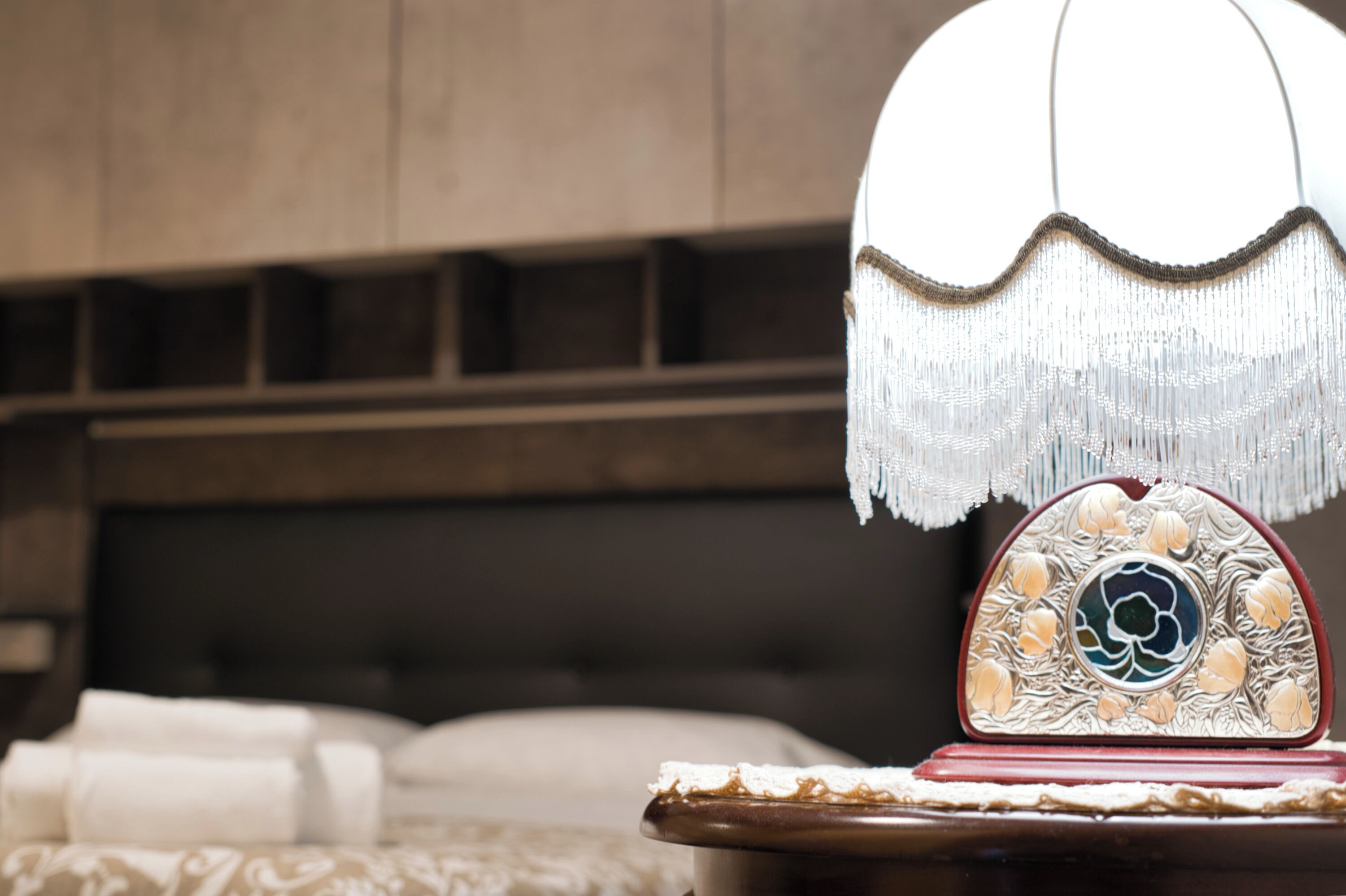A bed with white linens, a decorative lamp with a floral design, and a wooden headboard.