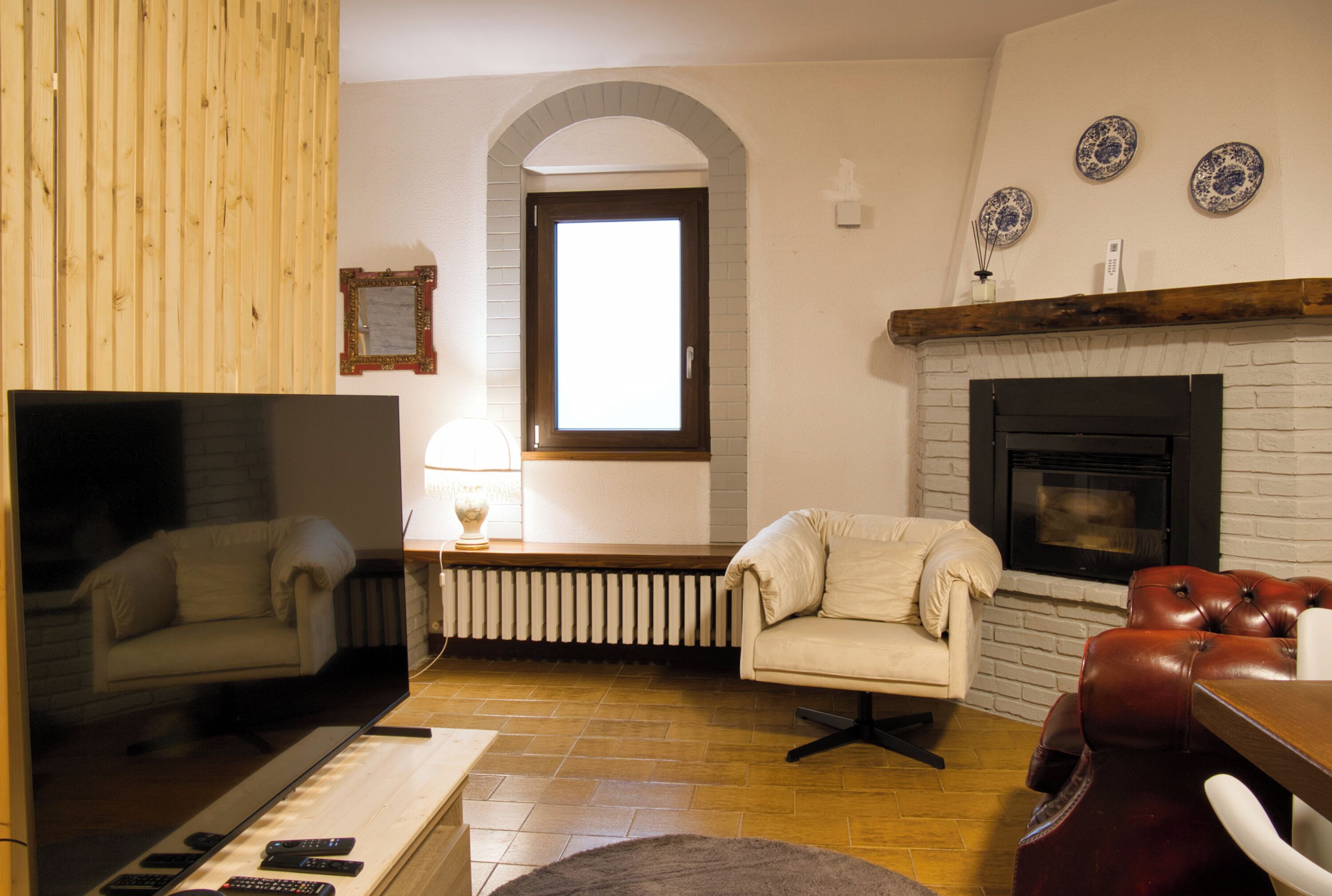 A living room with a TV, sofa, armchair, fireplace, and wooden wall paneling.