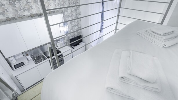 Una habitación de hotel moderna con una cama grande, vista a la ciudad a través de una ventana y un área de kitchenette.