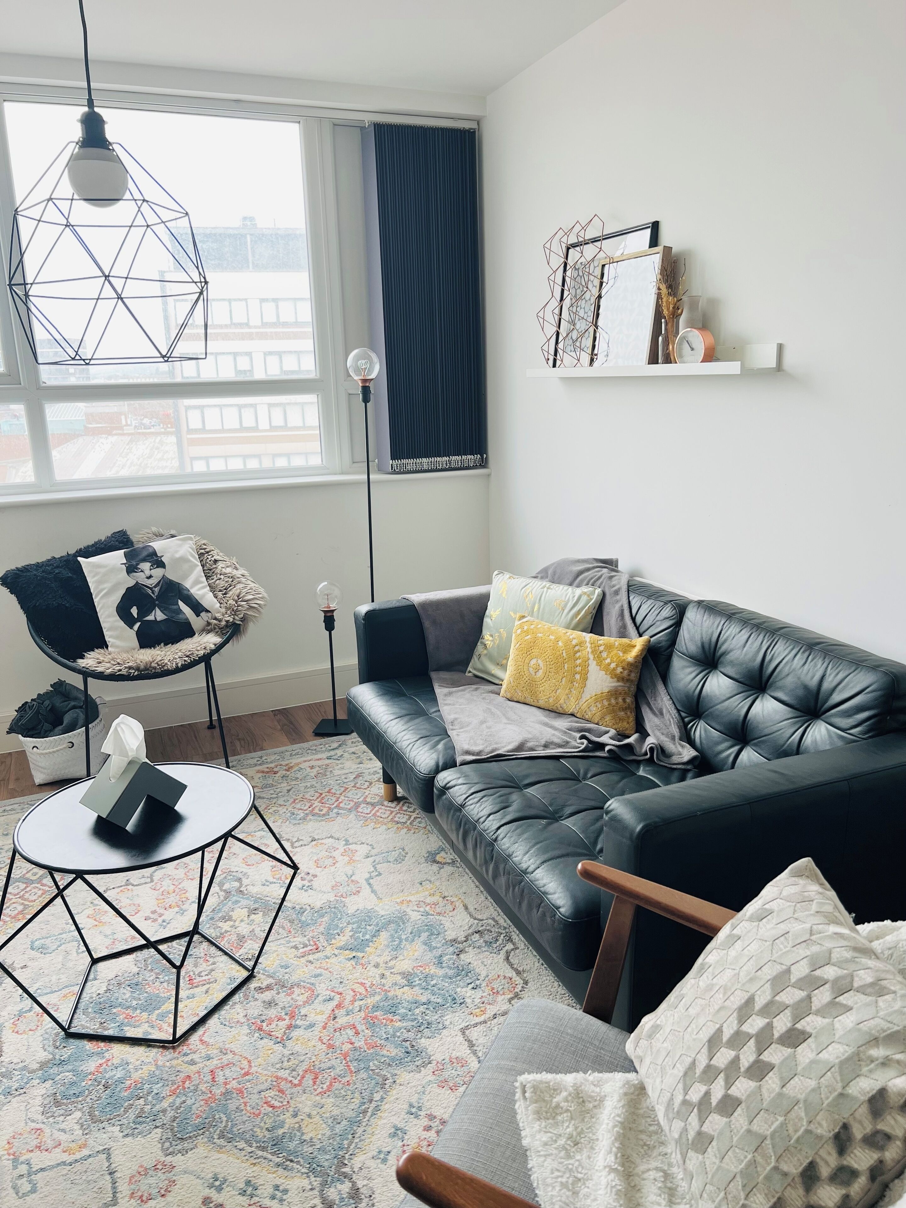 A modern living room with a leather sofa, a round coffee table, a chair, and a patterned rug.
