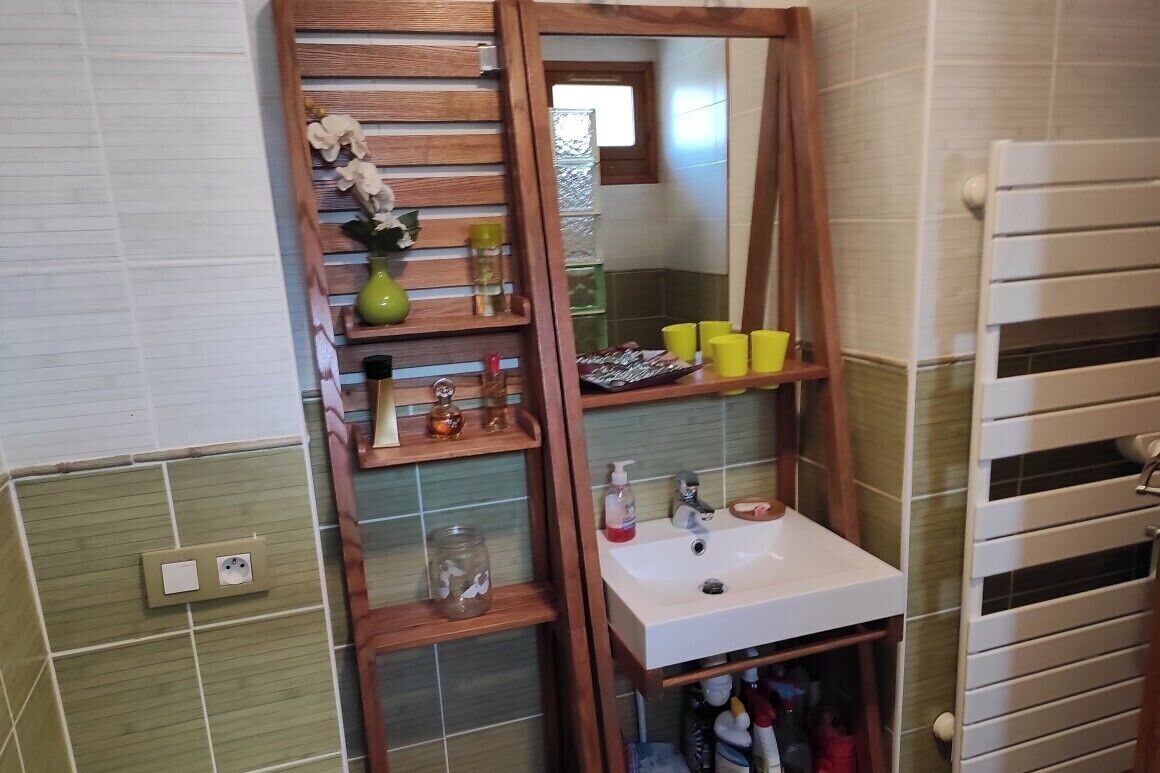 A bathroom with a wooden shelf unit, a white sink, and a mirror.