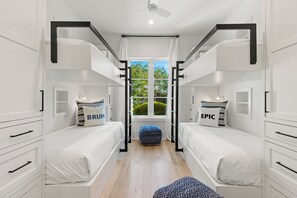 Un dormitorio moderno y bien iluminado con dos literas, una ventana con cortinas y un ventilador de techo.