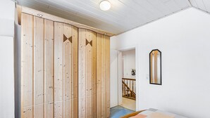 A bedroom with a wooden wardrobe, a bed with a quilt, a mirror on the wall, and a staircase leading to another room. - Knappstein Holiday Home with 4 Bedrooms, Garden, and Wi-Fi (Möhnesee)