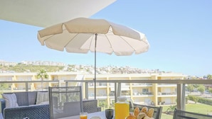 A balcony with a table set for breakfast, an umbrella, and a view of a residential area. - #323 Marina Apartment | Pool & Views (Albufeira)