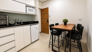 Une cuisine compacte avec des meubles blancs, un four à micro-ondes, une cuisinière et un réfrigérateur. On y trouve une table à manger en bois avec quatre chaises et une plante en pot.