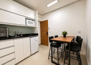 A compact kitchen with white cabinets, a microwave, a stove, and a refrigerator. There is a wooden dining table with four chairs and a potted plant. - Apartment Posto 5, close to the beach (Rio de Janeiro)