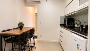 Une cuisine compacte avec un coin repas, des meubles blancs, un plan de travail noir et une petite plante en pot.