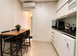 A compact kitchen with a dining area, white cabinetry, a black countertop, and a small potted plant. - Apartment Posto 5, close to the beach (Rio de Janeiro)