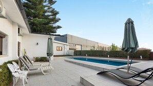 A modern outdoor pool area with lounge chairs, a small table, and umbrellas. - Casa São Domingos Lousada – Conforto e Vista Deslumbrante para a Vossa Família (Lousada)
