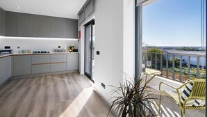 Une cuisine moderne avec des meubles gris, un plancher en bois et un balcon offrant une vue sur la ville.