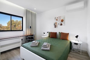 Een moderne slaapkamer met een bed, nachtkastjes, een bureau en uitzicht op bomen.