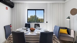 Un coin repas avec une table dressée pour quatre personnes, une fenêtre offrant une belle vue et un canapé agrémenté d’un coussin jaune.