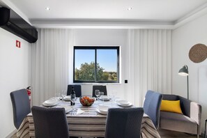 Ein Essbereich mit einem Tisch für vier Personen, einem Fenster mit Aussicht und einer Couch mit gelbem Kissen.