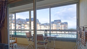 A balcony with a view of other buildings, a table, and two chairs. - Label Bleu - 300m de la plage (Courseulles-sur-Mer)