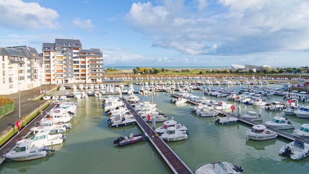 A marina with numerous boats docked, a long pier, and modern buildings in the background. - Label Bleu - 300m de la plage (Courseulles-sur-Mer)