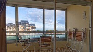 A balcony with a view of a building and a body of water. There are two chairs and a table. - Label Bleu - 300m de la plage (Courseulles-sur-Mer)