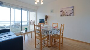A dining area with a round table, wooden chairs, and a view of the sea through large windows. - Label Bleu - 300m de la plage (Courseulles-sur-Mer)
