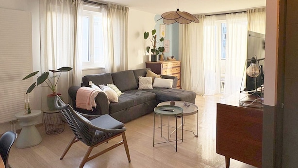 Ett modernt vardagsrum med en grå soffa, ett runt soffbord och en svart stol. På ett sidobord står en växt och på ett stativ står en lampa.