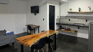 Uma cozinha moderna com uma mesa de madeira, cadeiras pretas, uma TV fixada na parede e uma porta que dá para outro cômodo.