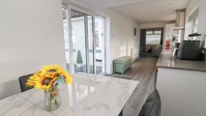 Eine moderne Küche mit Marmorarbeitsplatte, ein Essbereich mit Glastisch und Blick ins Freie durch große Schiebetüren.