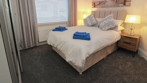 Ein ordentlich bezogenes Bett mit blauen Handtüchern, einer Nachttischlampe und einem Bild an der Wand.