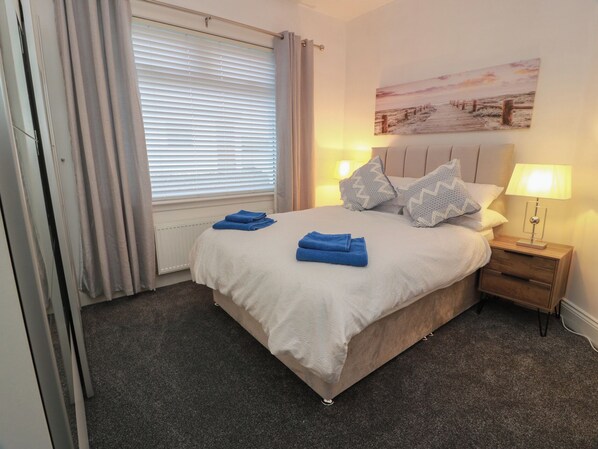 A neatly made bed with blue towels, a bedside lamp, and a painting on the wall.