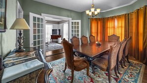 Ein Esszimmer mit einem großen Holztisch, sechs Stühlen, einer Kristallleuchter und einem gemusterten Teppich.
