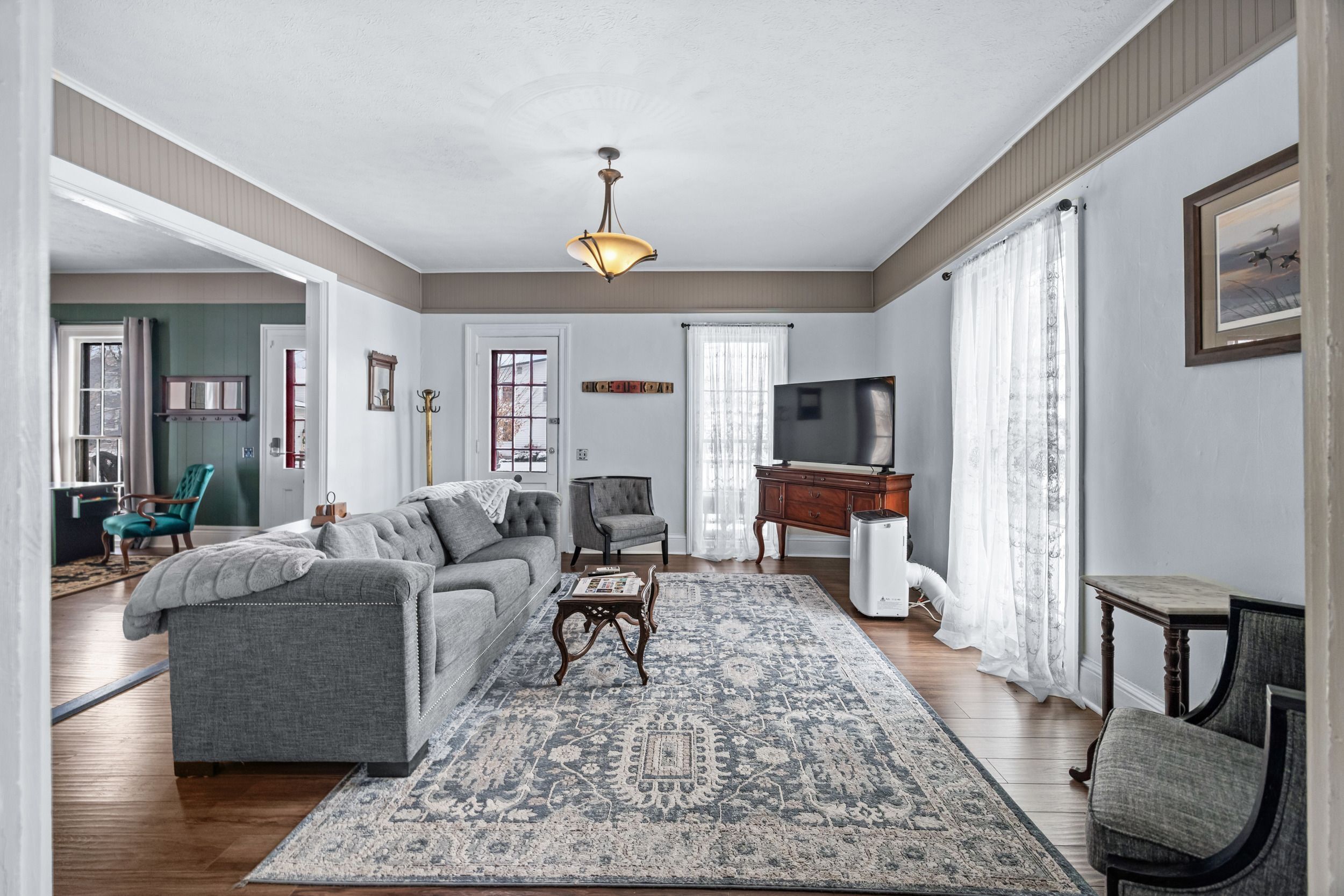 A spacious living room with a grey sofa, a patterned rug, a television, and a wooden cabinet.