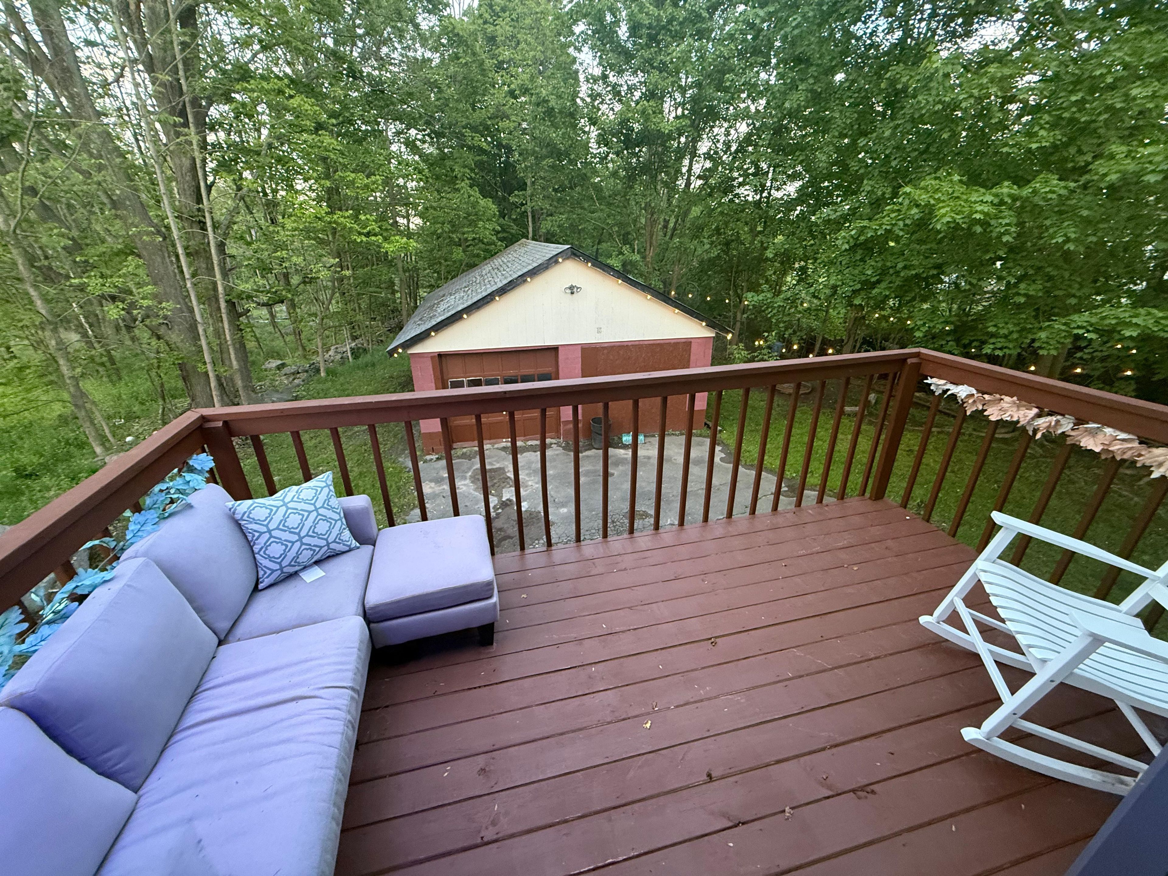 Une terrasse en bois avec un canapé et un fauteuil à bascule, d’où l’on peut admirer un petit bâtiment et une forêt dense.
