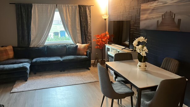 A modern living room with a sofa, a dining table, and chairs. There is a window with curtains, a lamp, and a painting on the wall. - The Resorts World Retreat Spacious 4-bedroom house in beautiful Monticello (Monticello)