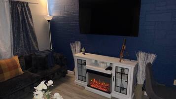 Ein Wohnzimmer mit Kamin, einer Couch, einem an der Wand befestigten Fernseher und einer Lampe.