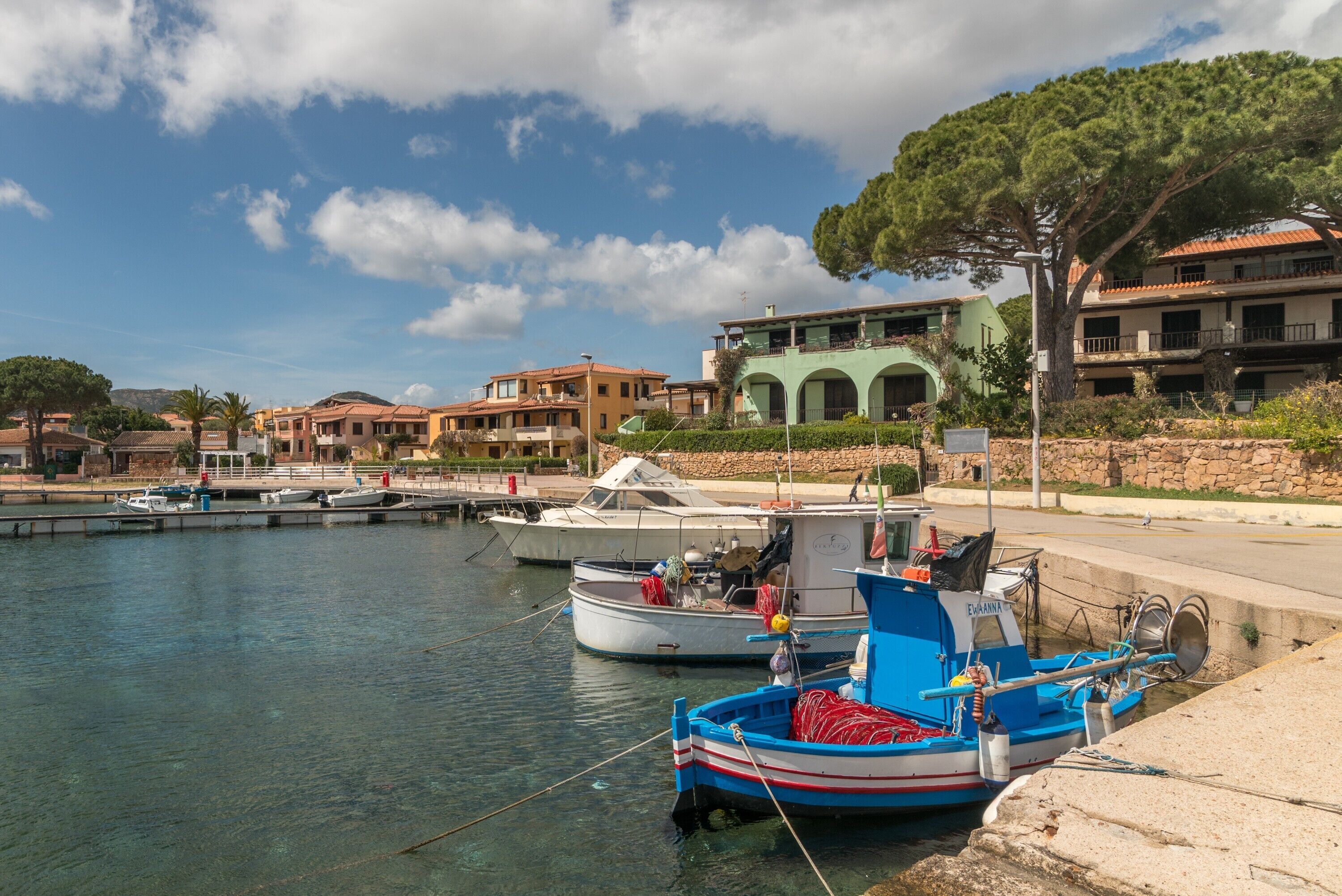 Un puerto deportivo con barcos amarrados, un muro de piedra y edificios con balcones.