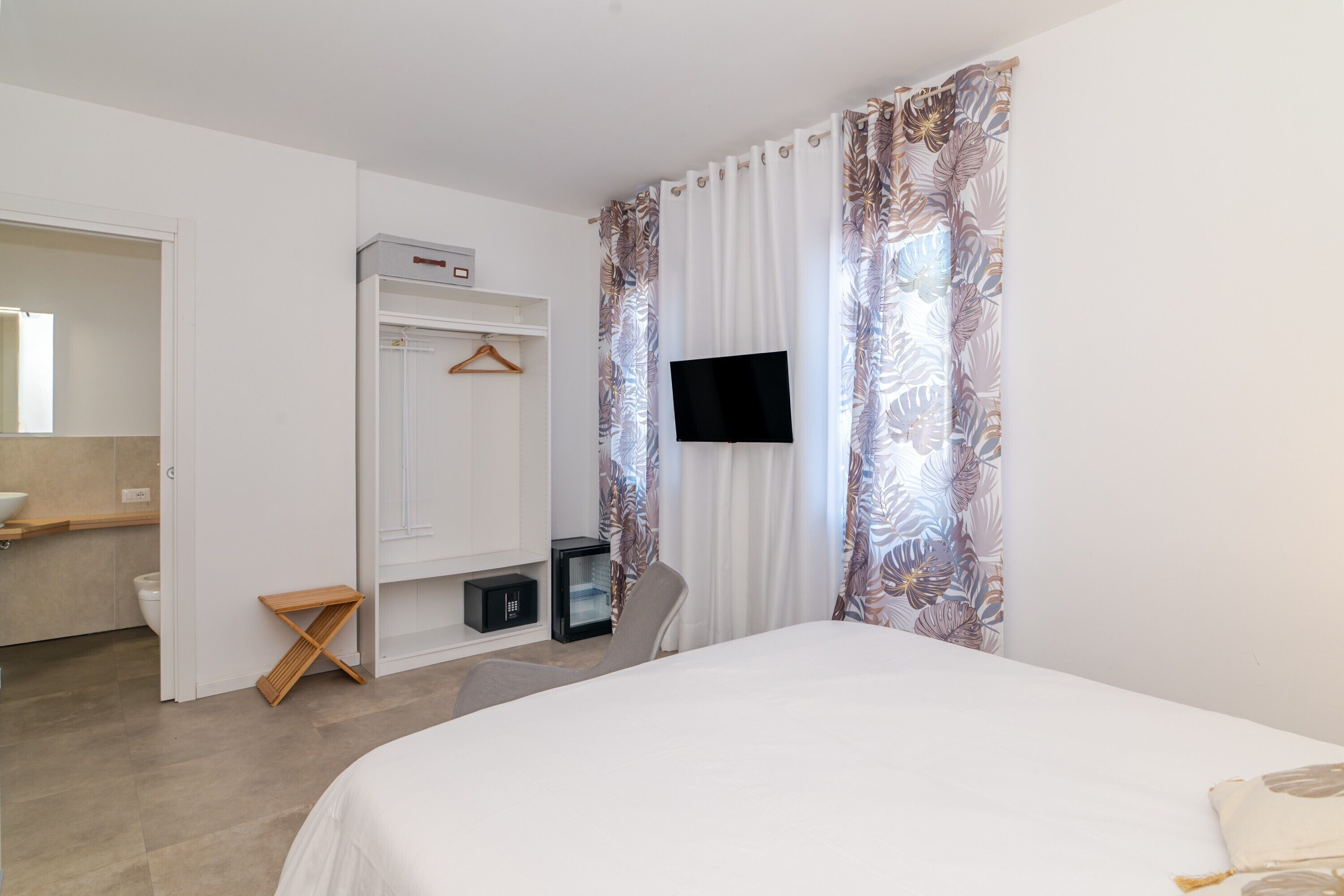 Un dormitorio con una cama, televisión instalada en la pared, armario, una mesita y un espejo.