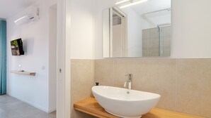 Une salle de bain moderne avec un lavabo blanc, un miroir et un téléviseur fixé au mur.