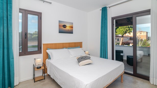 Une chambre à coucher comprenant un lit, une table de chevet, une fenêtre, un tableau et une porte-fenêtre coulissante donnant sur un balcon.